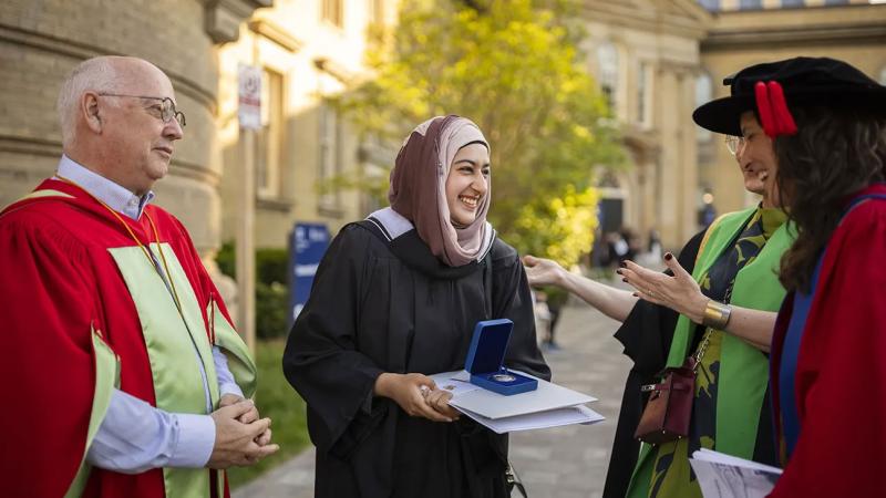 Hafsa Murtaza smiling at U of T officials as she holds her Governor General's Silver Medal