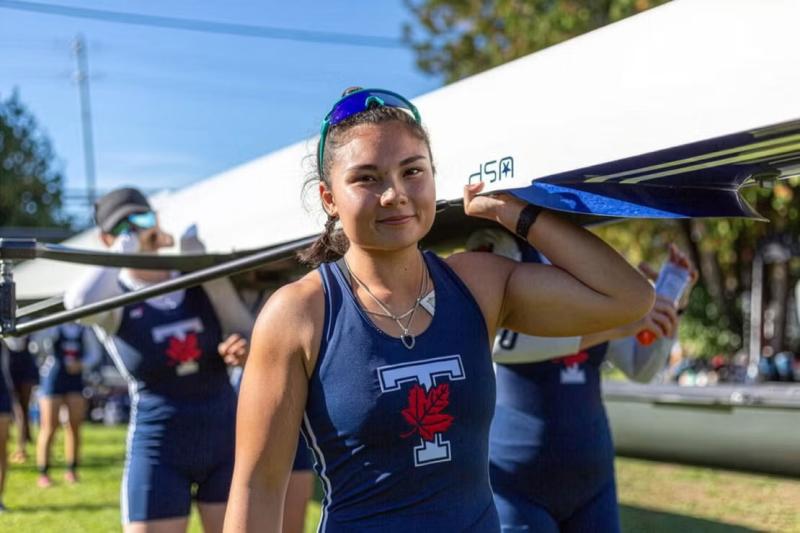 Vanessa Lin carrying a rowing boat on her shoulders with two other people in background