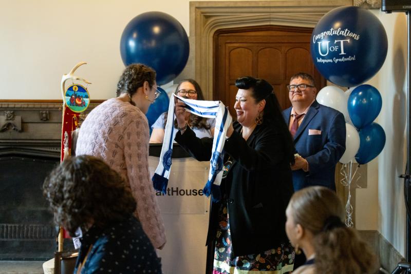 Jenny Blackbird presents Adrianna Lewis with an Indigenous stole at a May graduation celebration.